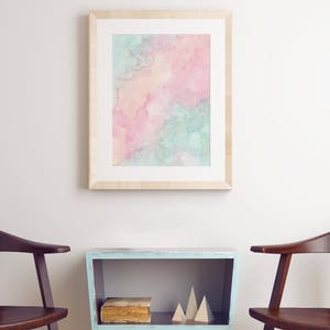 Puede incluir: Una pintura de acuarela enmarcada con tonos rosados, azules y amarillos cuelga sobre una mesa auxiliar azul claro con un libro y formas geom&eacute;tricas de madera. Dos sillas de madera flanquean la mesa.