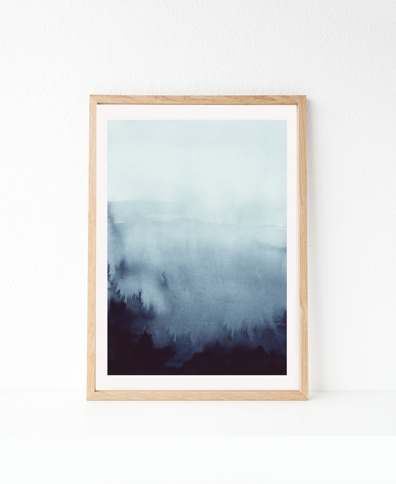 May include: A framed watercolor painting of a blue and gray landscape with a misty, foggy atmosphere. The painting depicts a forest scene with trees and hills in the background.