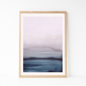 May include: A framed abstract watercolour painting with a soft, dreamy feel. The painting features a gradient of colours from light purple to dark blue, creating a sense of depth and movement. The frame is a simple, natural wood.