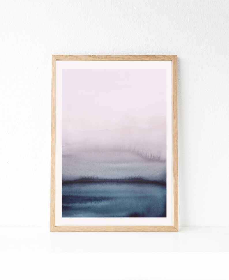 May include: A framed abstract watercolour painting with a soft, dreamy feel. The painting features a gradient of colours from light purple to dark blue, creating a sense of depth and movement. The frame is a simple, natural wood.