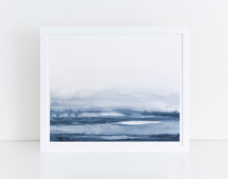 May include: A framed watercolor painting of a blue and white landscape. The painting features a hazy, abstract depiction of a mountain range and a body of water.