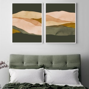 May include: Two abstract landscape prints with a green background and layered peach, brown, and gold shapes. The prints are framed in white and hung on a white wall.