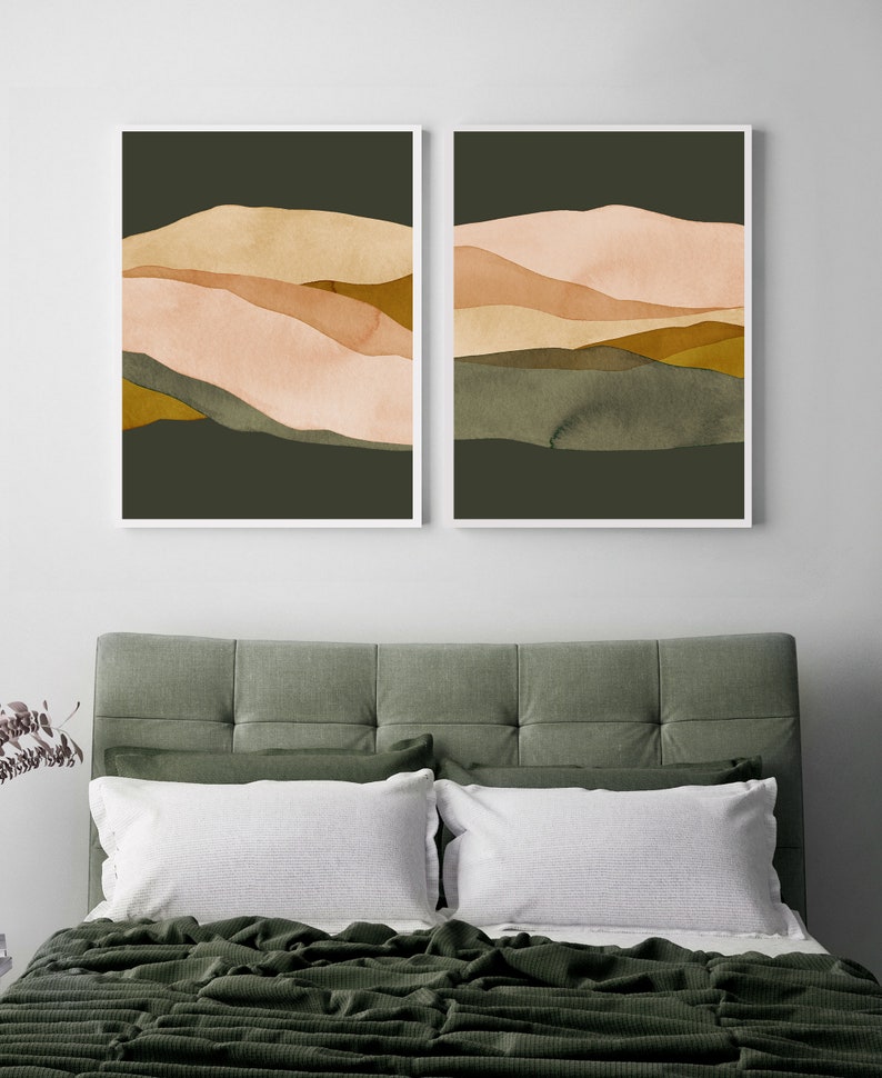 May include: Two abstract landscape prints with a green background and layered peach, brown, and gold shapes. The prints are framed in white and hung on a white wall.