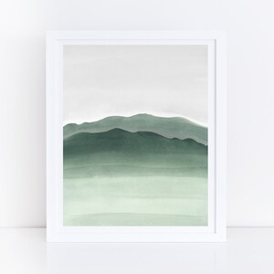 May include: A framed watercolor painting of a green mountain range with a light green sky. The painting is in a white frame.