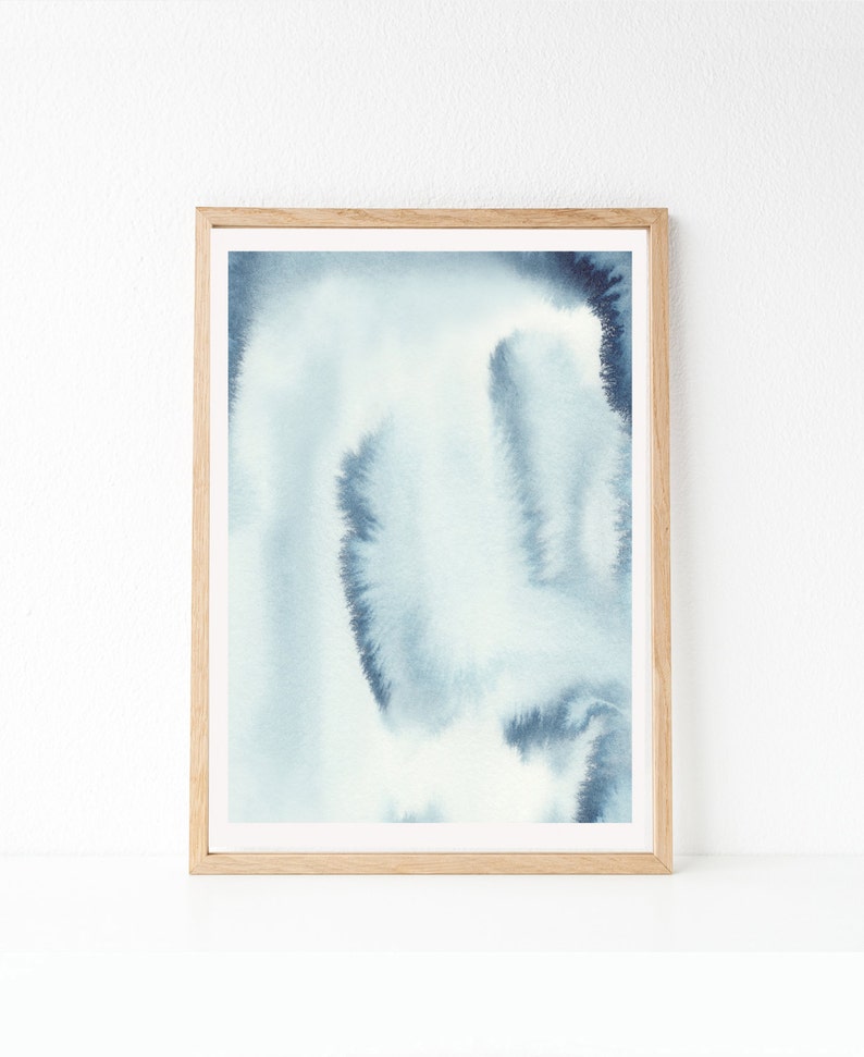 May include: A framed abstract watercolour painting with shades of blue and white. The painting has a soft, ethereal feel and is perfect for adding a touch of modern art to any room.