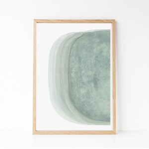 May include: A framed abstract art print with a light green watercolor design. The design features a curved shape with layers of color.