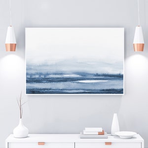 May include: A white dresser with two drawers and copper pulls. A blue and white abstract painting hangs above the dresser. Two copper pendant lights hang above the dresser. A white vase with a dried branch sits on the dresser. A white ceramic vase and a white plate are also on the dresser.
