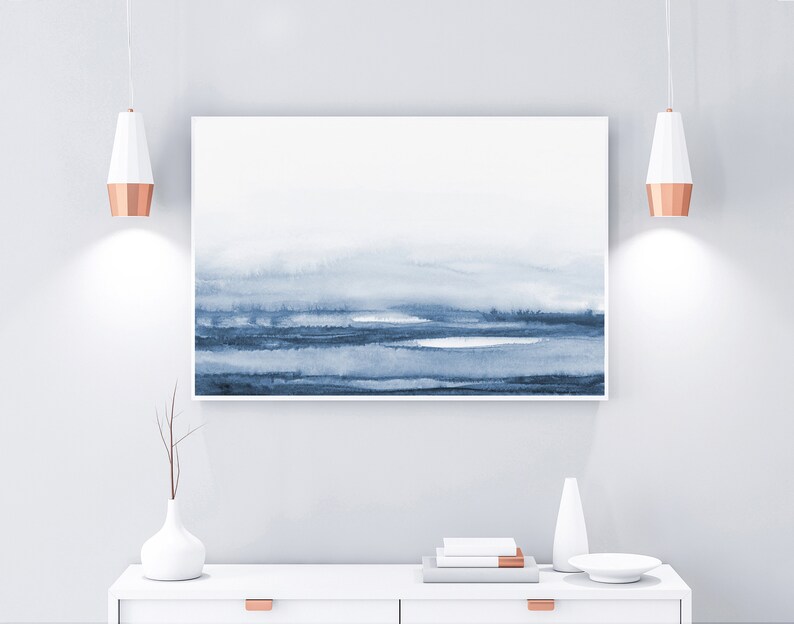 May include: A white dresser with two drawers and copper pulls. A blue and white abstract painting hangs above the dresser. Two copper pendant lights hang above the dresser. A white vase with a dried branch sits on the dresser. A white ceramic vase and a white plate are also on the dresser.