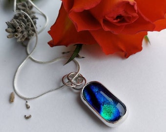 May include: A silver chain necklace with a pendant featuring a blue and green iridescent glass oval.