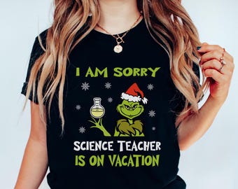 Pode incluir: T-shirt preto com o texto "I AM SORRY SCIENCE TEACHER IS ON VACATION". O design apresenta uma personagem de desenho animado verde com um gorro de Pai Natal e um béquer. Flocos de neve brancos espalhados.