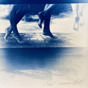 May include: A cyanotype print of two pairs of feet, one pair in mid-air and the other pair on a wooden floor. The background is a cloudy sky. The print is titled "Jump" and signed "Hall".