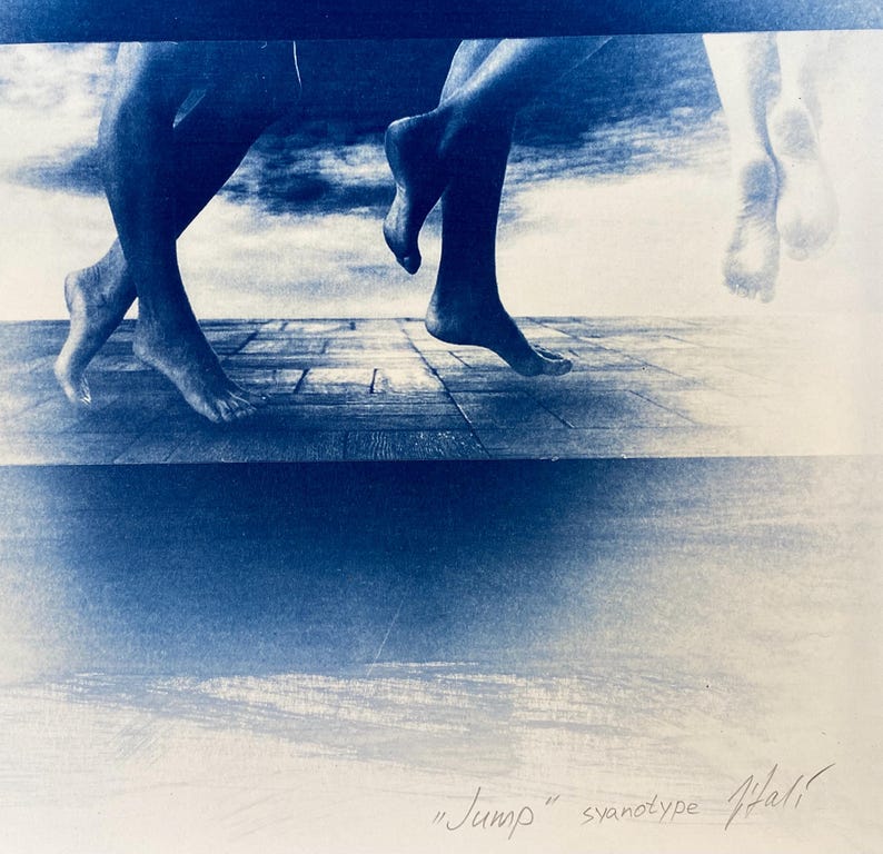 May include: A cyanotype print of two pairs of feet, one pair in mid-air and the other pair on a wooden floor. The background is a cloudy sky. The print is titled "Jump" and signed "Hall".