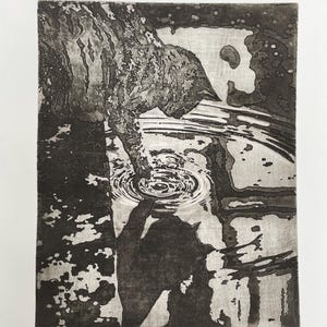 May include: A black and white etching print depicting a cat reaching into water, creating ripples. The print has a textured appearance, with the cat's fur and the water's surface detailed. The title "The art of light touches" is at the bottom.