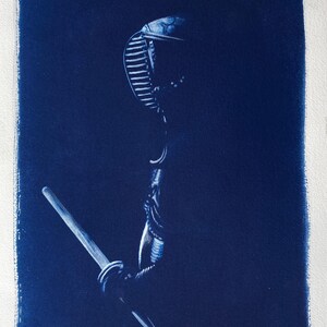 May include: A blue and white cyanotype print of a person wearing a kendo helmet and holding a sword. The image is titled "Kendo" and signed "E.A. Mali".