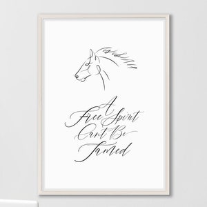 May include: A white framed print with a black line drawing of a horse's head and the text "A free spirit can't be tamed". The print is hanging on a white wall above a white desk with a white laptop and a white chair.
