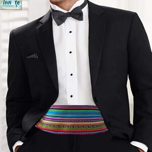Puede incluir: Chaqueta de esmoquin negra con camisa blanca, pajarita negra y fajín tejido colorido. El fajín presenta rayas horizontales en rojo, azul, verde y morado.