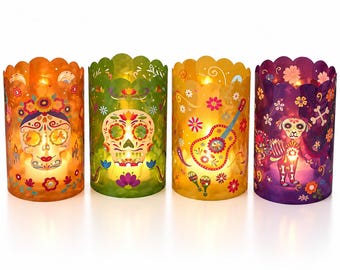 May include: Four cylindrical candle holders with scalloped edges, featuring vibrant designs including sugar skulls, a guitar, maracas, and a dog. Each translucent holder is illuminated from within, displaying orange, green, yellow, and purple colours.