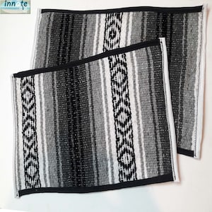 May include: Two black and white striped woven placemats with black trim. The placemats are made of a soft, textured fabric.