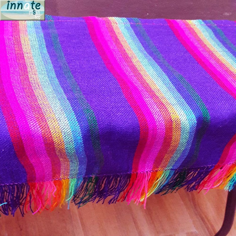 May include: A vibrant, striped textile in shades of purple, pink, red, orange, yellow, green, and blue. The fabric has a fringed edge. The Innate Hisan Shop logo is in the upper left corner.
