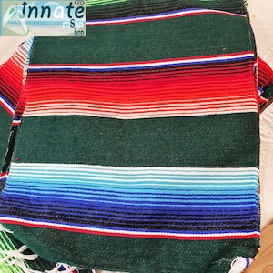 May include: A colorful striped blanket with green, red, white, blue, and black stripes. The blanket is made of woven fabric and has a fringed edge.