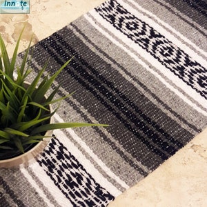 May include: A woven runner rug featuring a striped pattern in shades of black, charcoal gray, and white. The textile displays alternating bands of solid colors and intricate geometric diamond motifs, creating a textured surface with a visible weave.