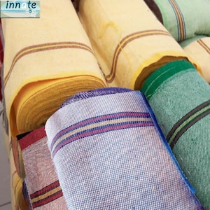 Puede incluir: Primer plano de varios rollos de tela con rayas de diferentes colores. Las telas son amarillas, verdes, azules y rojas.