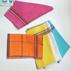 Puede incluir: Cinco servilletas de tela en varios colores y patrones. Las servilletas están dobladas y dispuestas sobre una superficie blanca. Las servilletas son de color naranja con rayas negras, amarillas con rayas multicolores, blancas con rayas multicolores, azul claro con rayas multicolores y rosas con rayas multicolores.