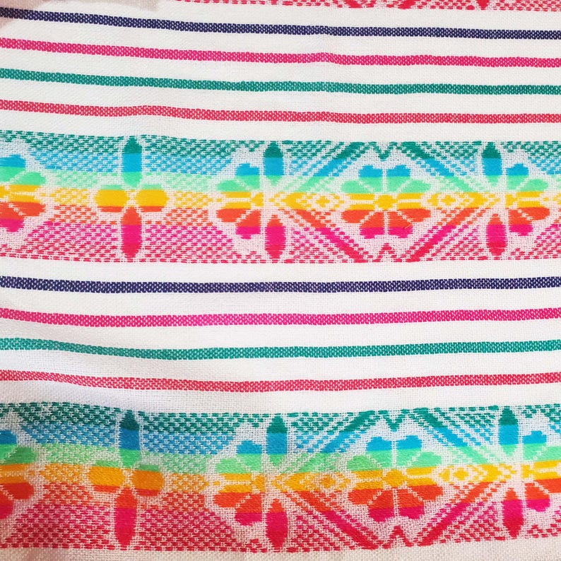 May include: A colorful textile with a white background, featuring horizontal stripes in red, green, and blue. The design includes vibrant floral patterns in rainbow hues, creating a lively and decorative look.
