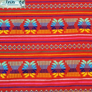 May include: Red fabric with a colourful geometric pattern. The pattern features blue, green, yellow, and white stripes and a repeating design of stylised flowers.