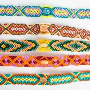 May include: Five colorful friendship bracelets with different geometric patterns and a decorative bead in the center of each bracelet.