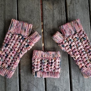 May include: A pair of pink and blue fingerless gloves and a matching wrist warmer, all crocheted with a textured stitch.