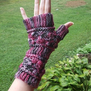 May include: Pink, black, and gray fingerless gloves with a textured knit pattern. The gloves have a long cuff and a fingerless design.