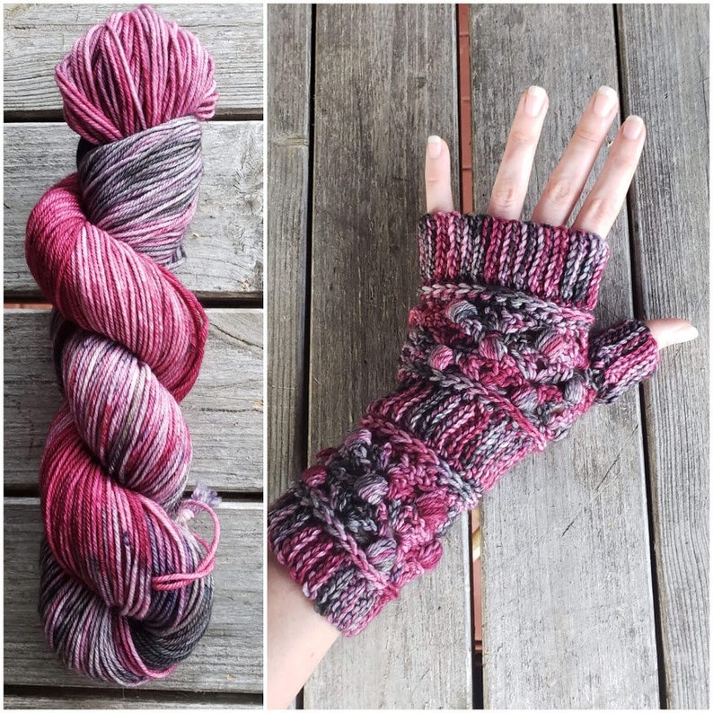 May include: A skein of yarn in shades of pink and gray. The yarn is twisted into a spiral shape. A knitted fingerless glove in the same colors is shown in the background.