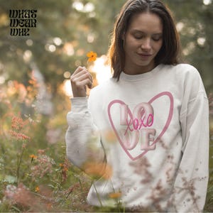 May include: White sweatshirt with a pink heart graphic and the text "Love xoxo" inside the heart.