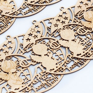 May include: Multiple circular light brown wooden ornaments featuring a laser-cut design of an angel with wings and a halo, surrounded by stars and crescent moon shapes. Each piece includes the text "Jose Maria" and a small loop for hanging.