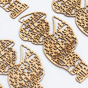 May include: Multiple light brown wooden laser-cut ornaments shaped like angels. Each ornament features a halo and intricate cut-out text forming the body and wings, with the words 'Angel de la guarda' and 'Amen' clearly visible in the design.