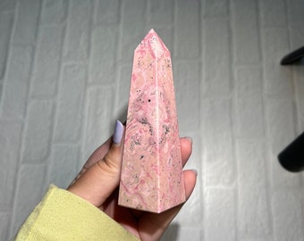 May include: A pink and white crystal point with a pointed top and a smooth, polished surface. The crystal has a swirling pattern of pink and white.