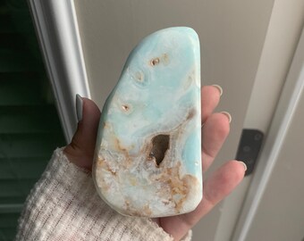 May include: A light blue and brown polished stone with a unique swirling pattern. The stone is smooth and has a natural, organic shape.