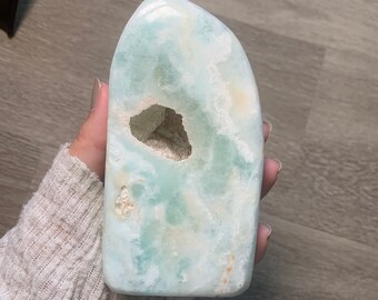 May include: A light blue and white celestite crystal with a natural hole in the center. The crystal is smooth and polished, with a unique, organic shape.