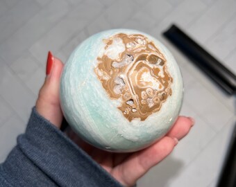 May include: A light blue and brown sphere with a swirling pattern. The sphere is made of a natural material, possibly a type of agate or jasper.