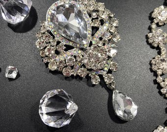 May include: A silver bridal belt with a large teardrop-shaped crystal pendant and smaller crystals throughout. The belt is adorned with a delicate floral design.