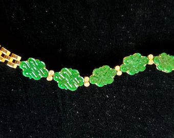 May include: A gold chain bracelet with green jade charms in the shape of a knot. The charms are spaced evenly along the chain.