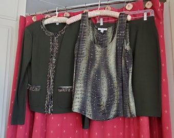 May include: A green blazer with a ruffled trim, a green and brown patterned tank top, and a green skirt. The clothing is hanging on hangers against a red background.