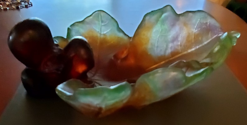May include: A decorative glass bowl in the shape of a leaf, with a dark brown center and a translucent green and yellow rim. The bowl has a unique, organic design, perfect for displaying small items.