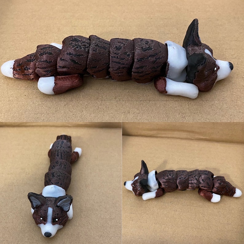 May include: A brown and white dog figurine with segmented body parts, lying on its side with its head turned to the side. The figurine is made of a textured material that resembles fur.