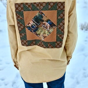 Puede incluir: Una camisa de botones de color tostado con un dise&ntilde;o de patchwork en la espalda. El patchwork es un cuadrado con un patr&oacute;n marr&oacute;n, verde y blanco. El centro del patchwork presenta una impresi&oacute;n de ciervos en un entorno de bosque.
