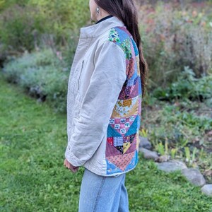 May include: A beige jacket with a patchwork design on the back. The jacket is made of a soft, comfortable fabric and has a relaxed fit. The patchwork design is made up of different colored fabrics, including blue, green, red, and yellow.