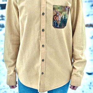 Puede incluir: Una camisa de manga larga de color beige claro con botones y un bolsillo con estampado de ciervo. La camisa tiene un corte holgado y est&aacute; hecha de una tela suave y c&oacute;moda.