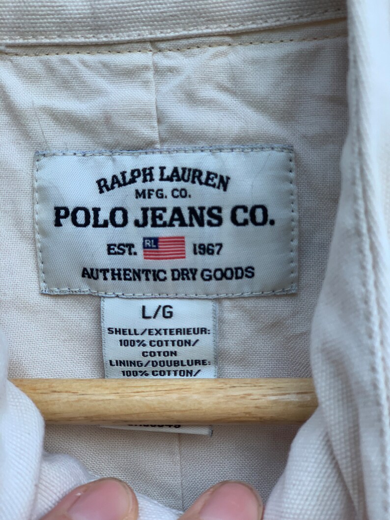 May include: A white label with black text that reads "Ralph Lauren Mfg. Co. Polo Jeans Co. Est. 1967 Authentic Dry Goods" and "L/G Shell/Exterieur: 100% Cotton/Coton Lining/Doublure: 100% Cotton/"