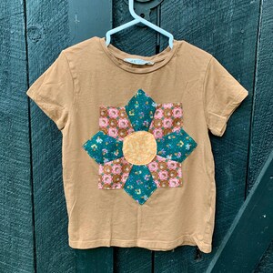 May include: A brown short-sleeved t-shirt with a colourful patchwork flower design on the front.